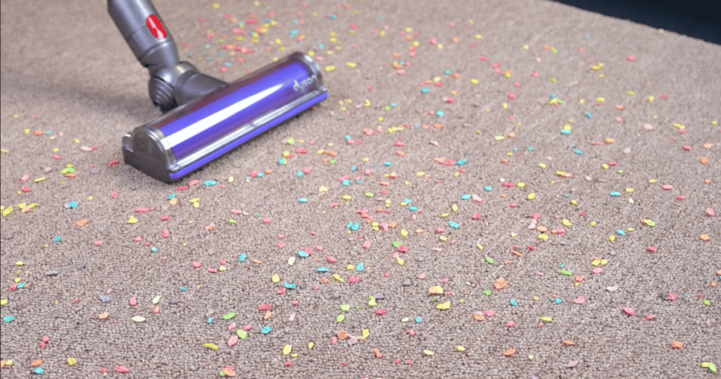 Cordless vacuum picking up colorful debris on carpet.