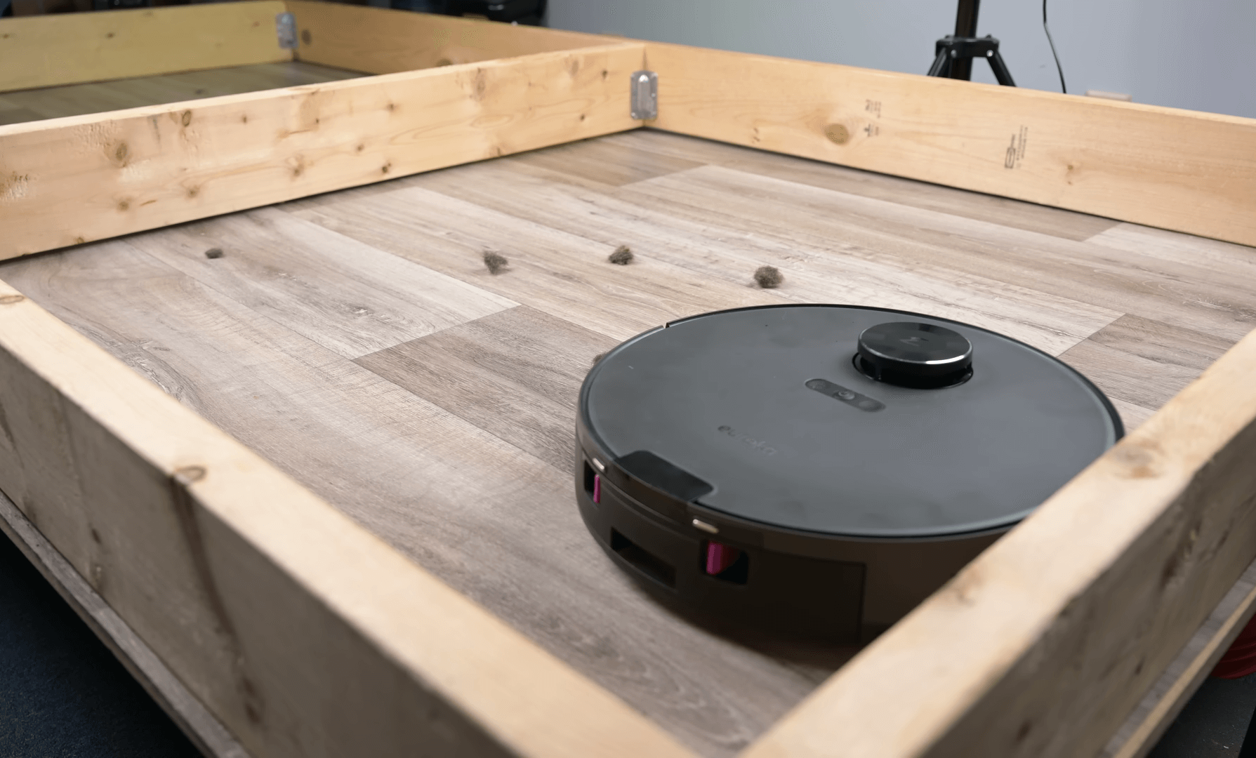 A black Eureka E10S robotic vacuum cleaner is in the middle of a wooden floor with a noticeable amount of hair around it