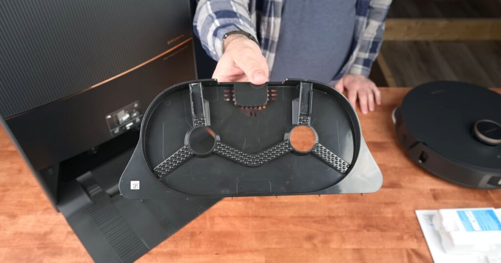 Close-up of a hand holding the Dreame robot vacuum’s removable drip tray from the dock base.