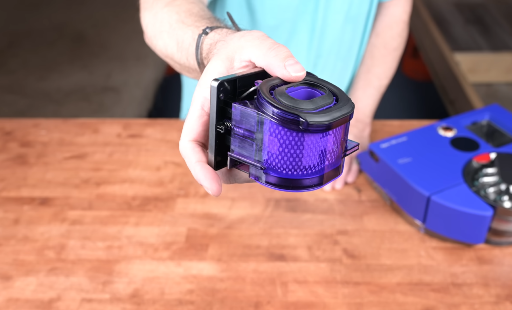 Close-up of a hand holding the Dyson 360 Vis Nav's HEPA filter, showcasing its purple hue and cylindrical design.