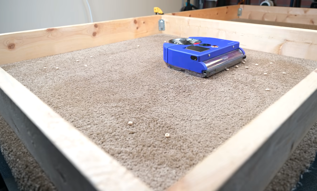 The Dyson 360 Vis Nav robot vacuum cleaning a carpet scattered with larger debris in a controlled testing environment.