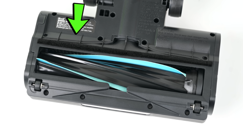 Close-up view of the underside of the Levoit LVAC-200 vacuum's floorhead, showing its brush roll and cleaning combs. A green arrow points to the active hair removal combs and soft felt squeegee.