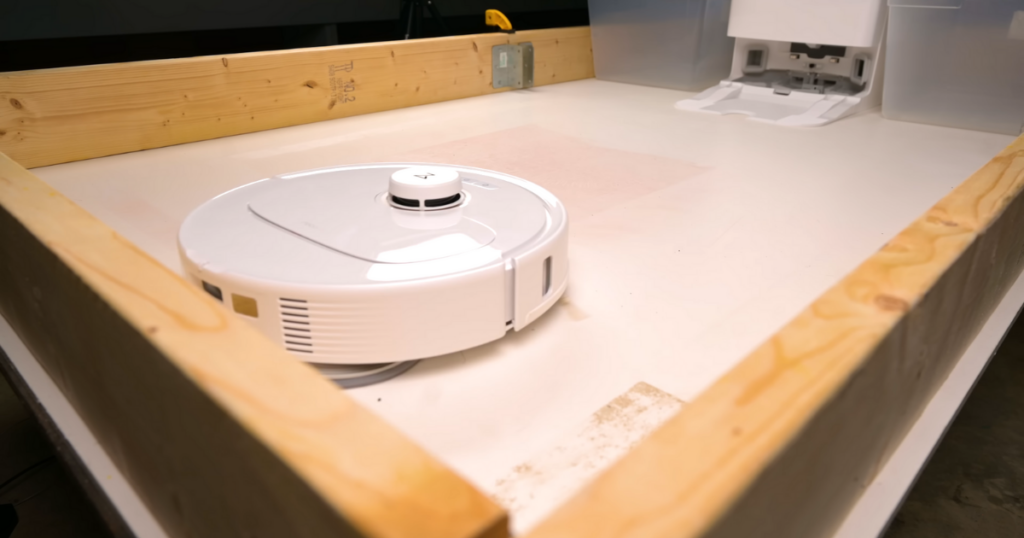 Q Revo MaxV robot vacuum operating in a test area with wooden borders, moving away from its charging dock.
