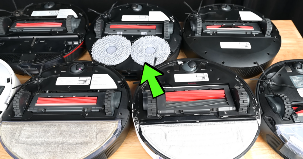 Several robot vacuums are shown upside down, displaying their brushes and mop pads. A green arrow highlights the spinning mop pads of the Q Revo MaxV.