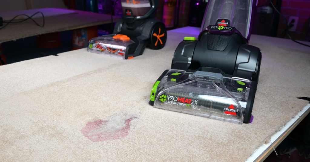 The Bissell 2X Revolution Pet Pro carpet cleaner in action, showcasing its "Clean Shot" technology for targeted stain treatment on a beige carpet.