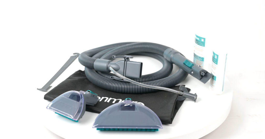 A set of carpet cleaner attachments including a long hose, two different cleaning heads, a cleaning tool, a storage bag, and bottles of cleaning solution.