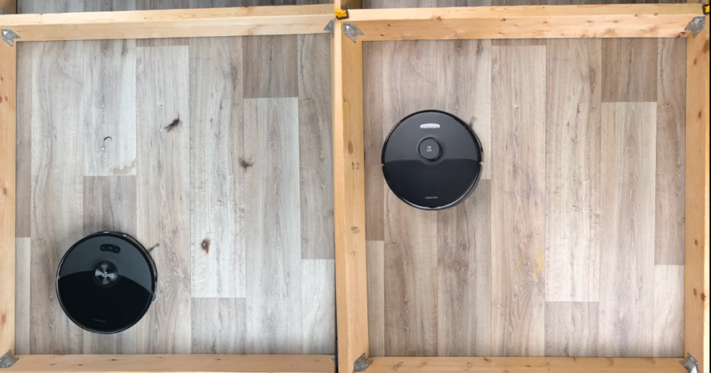 Two Roborock robot vacuums, the S8 Max Ultra (left) and the S8 MaxV Ultra (right), in separate wooden frame enclosures on a wood-patterned floor. Each vacuum is actively cleaning, surrounded by scattered debris.