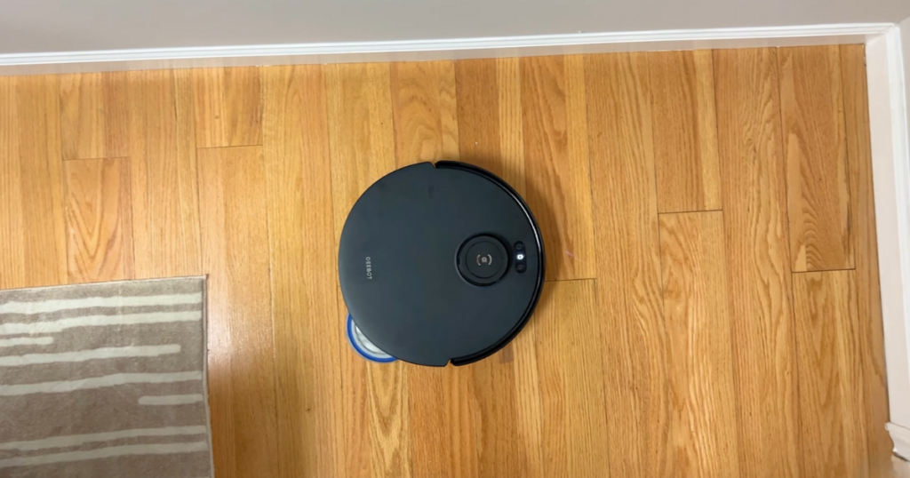 Deebot T30S robot vacuum cleaning a hardwood floor next to a rug, demonstrating the TruEdge feature, viewed from above.