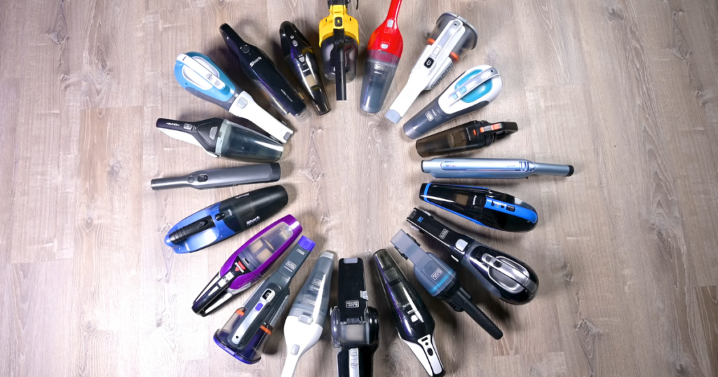 A variety of handheld vacuum models arranged in a circle on a wooden floor.