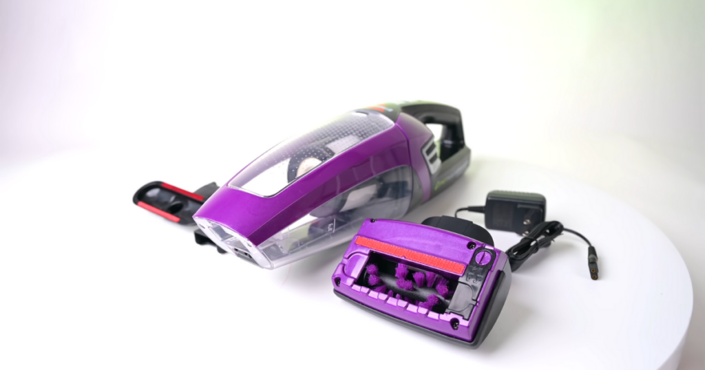 A close-up of a purple Bissell Pet Hair Eraser handheld vacuum cleaner with a detachable motorized turbo brush attachment and charging cable, all placed on a white surface.