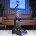 Bissell TurboClean Pet XL 150 | Vacuum Wars Blue and black upright floor cleaning machine with handle, standing on a rug in a living room near a sofa.