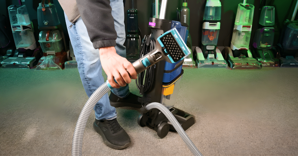 Close-up of a person using an upright vacuumโs flexible hose attachment for above-floor cleaning in a testing lab.
