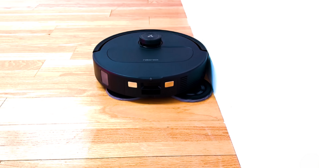 Qrevo Master robot vacuum and mop cleaning along the edge of a wall on a wooden floor.