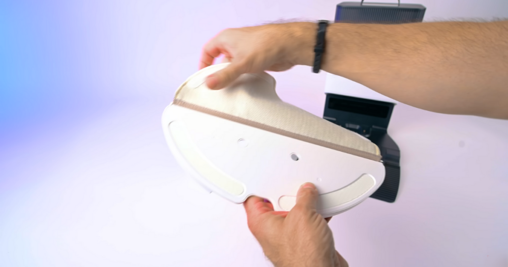 A close-up of a person’s hands attaching the mop pad to the bottom of the Roborock Q8 Max+ robot vacuum. 