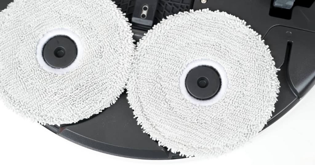 A close-up view of the underside of the Samsung Bespoke Jet Bot AI Combo robot vacuum, showing two circular microfiber mop pads attached to the device.