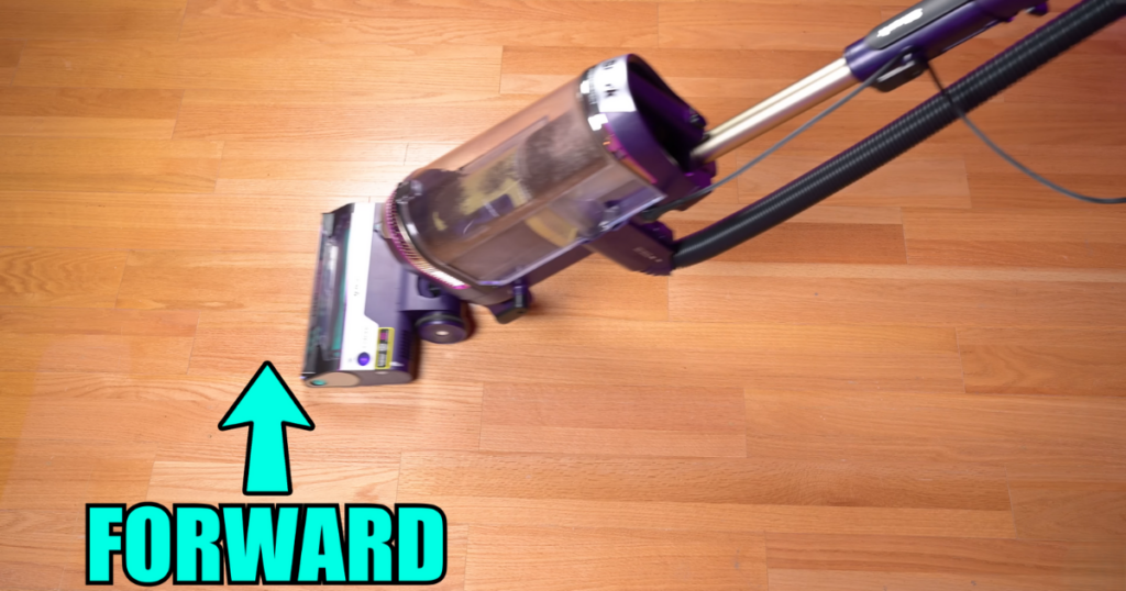 Shark PowerDetect vacuum in action on a hardwood floor, demonstrating its Direction Detect feature. An arrow points in the forward direction, labeled with the word "FORWARD."