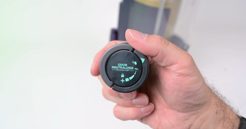 Close-up of a hand holding the Shark PowerDetect vacuum's Odor Neutralizer cartridge. The cartridge features a dial for adjusting the intensity of the odor-neutralizing technology.