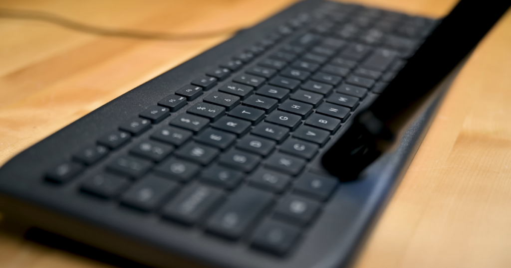 A close-up view of a black computer keyboard being cleaned with a brush attachment.