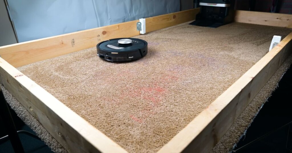 Shark NeverTouch Pro robot vacuum performing a carpet debris pickup test on a controlled test bed with visible scattered debris.