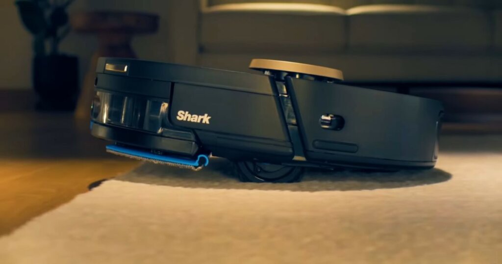 Shark NeverTouch Pro robot vacuum lifting its mop pad while transitioning from a hard floor to a carpeted surface.