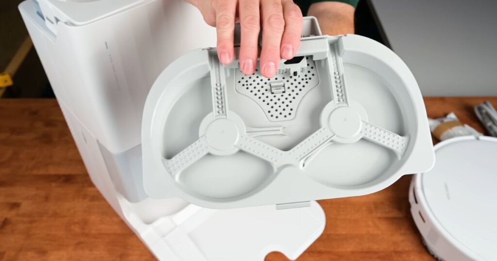 A person holding the removable mopping tray from the Roborock QRevo Edge dock. The tray has two circular mop pad holders and a perforated section for water drainage.