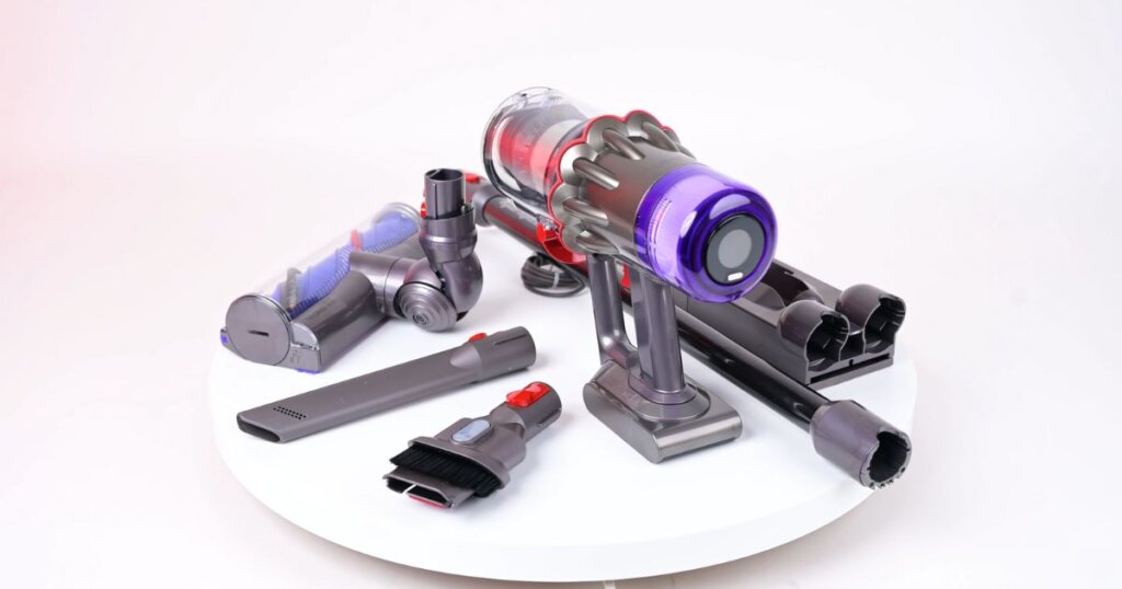 Dyson Digital Slim cordless vacuum displayed with all included accessories, including a crevice tool, brush attachment, charging dock, and cleaner head.