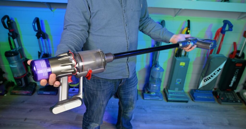 Person holding the Dyson Digital Slim cordless vacuum in a testing room with other vacuums in the background, highlighting its lightweight build.