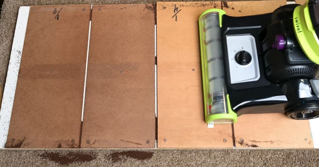 Vacuum cleaner on a wooden test panel with four sections labeled for crevice pick up testing. There are visible debris.