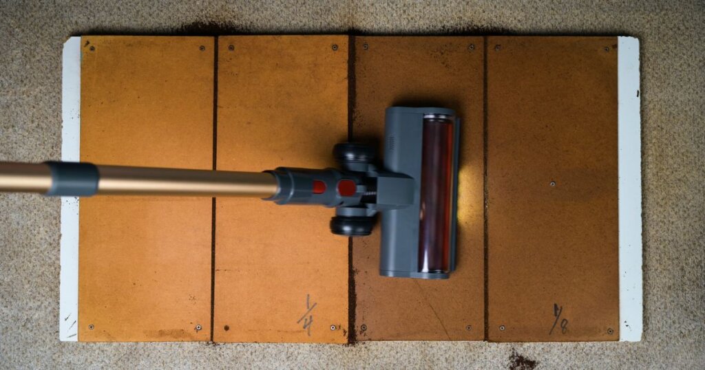 Vacuum head shown during a crevice pickup test on a hard floor with visible dirt accumulation.