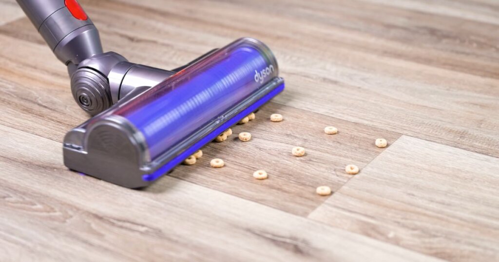 A vacuum cleaner head pushing cereal pieces across a hard floor, demonstrating the snowplow effect.