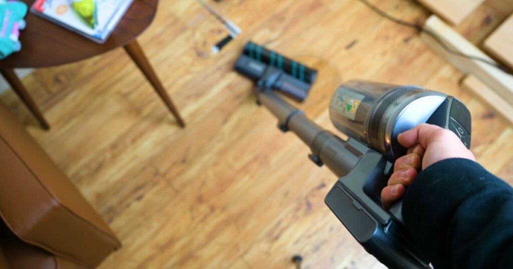 Top-down view of a person using a cordless vacuum on hardwood flooring with a soft roller head.