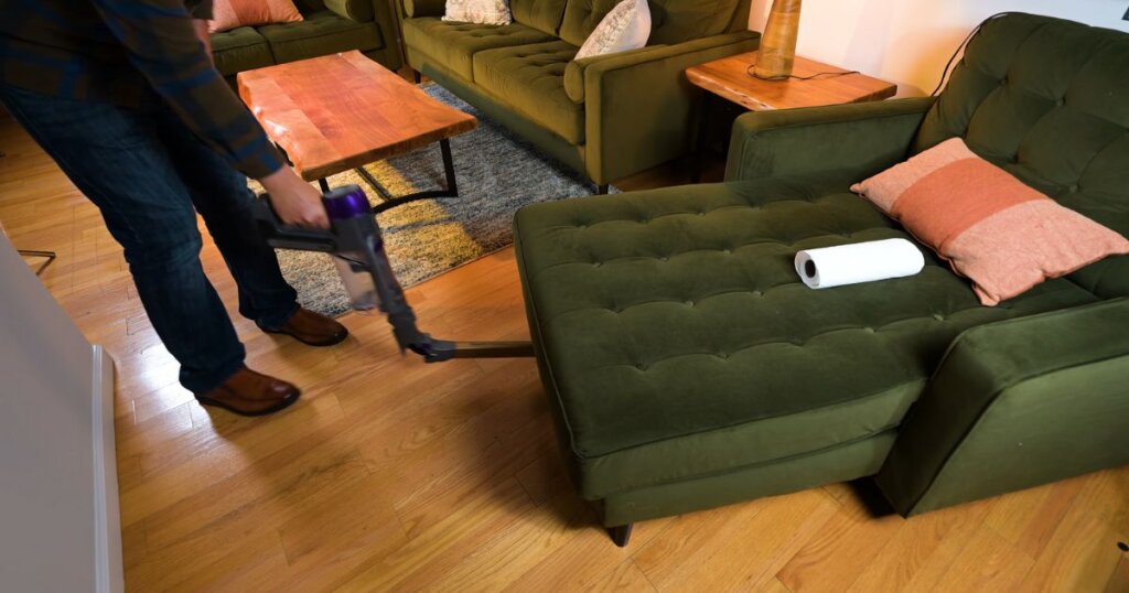 User vacuuming under a chaise lounge using a cordless vacuum with a pivoting wand for low-clearance access.