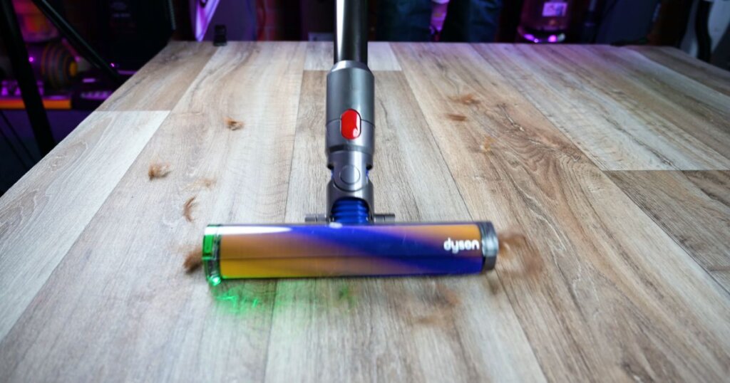 Dyson soft roller head picking up pet hair from a hardwood floor, illuminated by green LED.