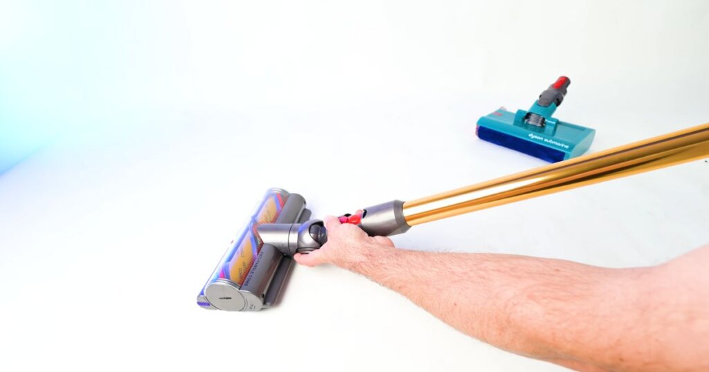 A user manually swaps between a soft roller and another vacuum head on a cordless stick vacuum.