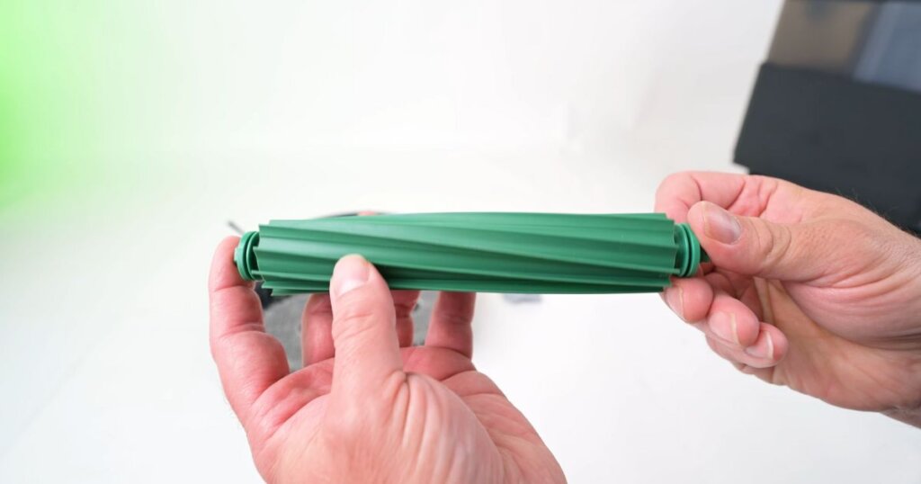 Close-up of a hand holding the green single brush roller used in the Roomba Plus 405 Combo robot vacuum.