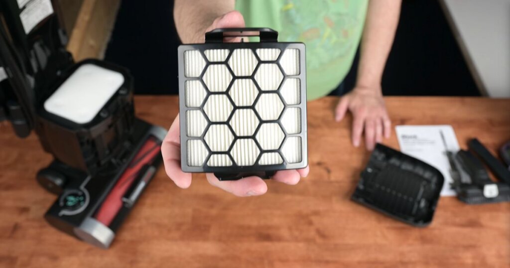 HEPA filter module being held in hand with the Shark vacuum base in the background.