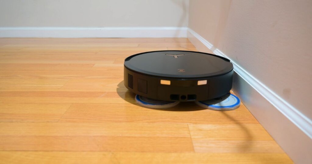 Side view of an Ecovacs T50 robot vacuum extending its mop pads while hugging a baseboard, demonstrating the TrueEdge mopping system in action.