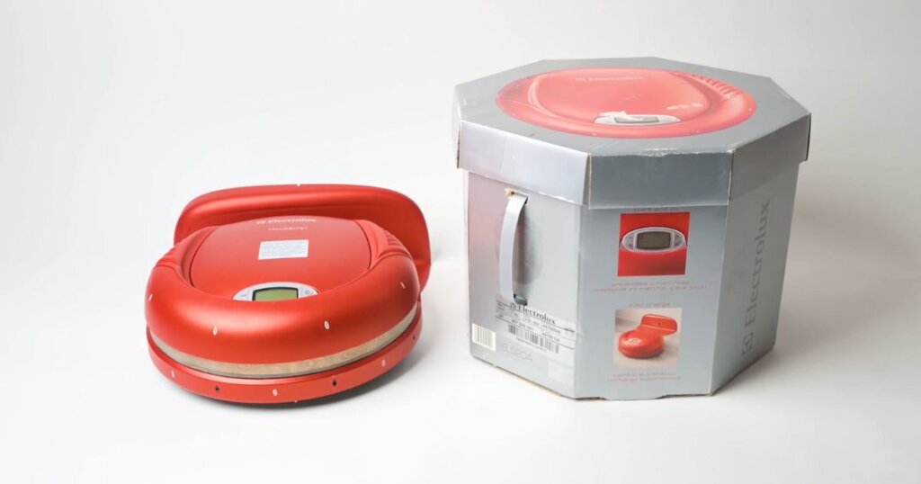 A red Electrolux Trilobite robot vacuum beside its octagonal packaging, showing the first commercially available robot vacuum model.