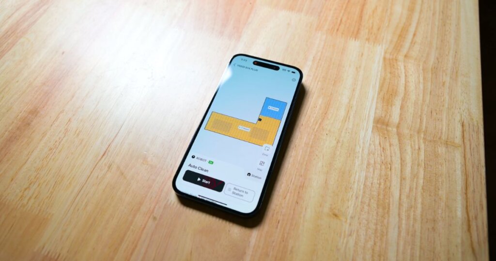 Smartphone showing the Yeedi app’s mapping and room control interface on a wooden surface.