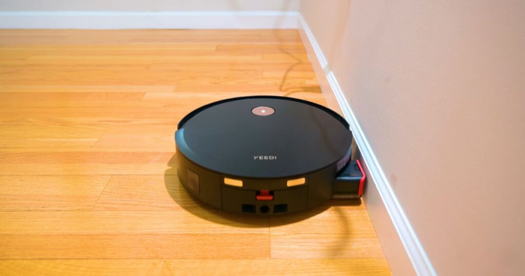 Yeedi S14 Plus vacuum cleaning along a baseboard, demonstrating automatic roller module extension for edge coverage.