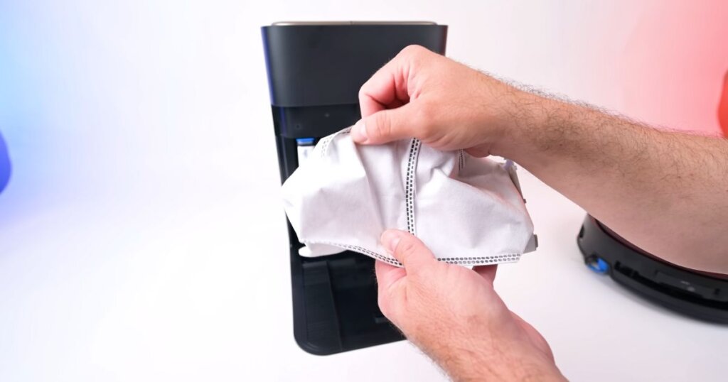 Person holding a 3-liter disposable dust bag for the Ecovacs X9 Pro Omni, positioned in front of the dock.