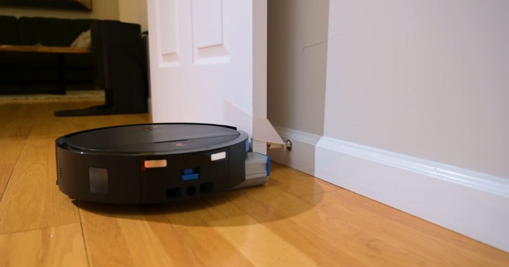 Ecovacs Deebot X9 Pro Omni robot vacuum extending mop arm near baseboard corner and doorstop.
