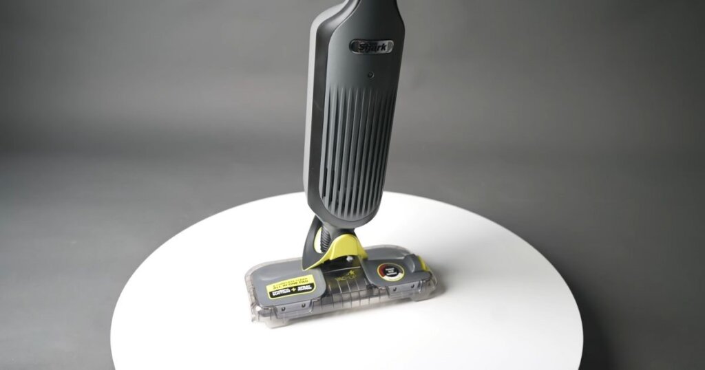 Shark VACMOP is displayed upright on a white circular platform, highlighting the front design of the unit. 