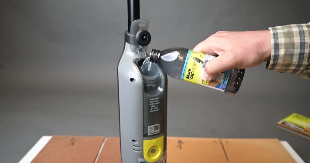 Hand pouring Shark VACMOP floor cleaner solution into the water tank of the Shark VACMOP device.