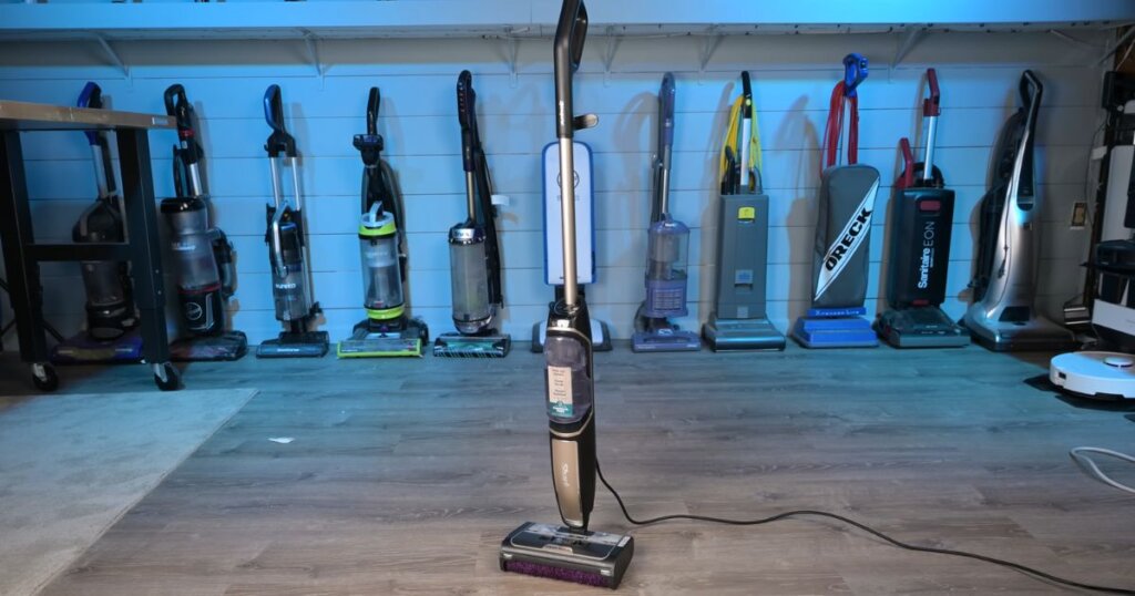 Full view of the Shark Steam Pickup upright in a test room surrounded by other vacuums in the background.