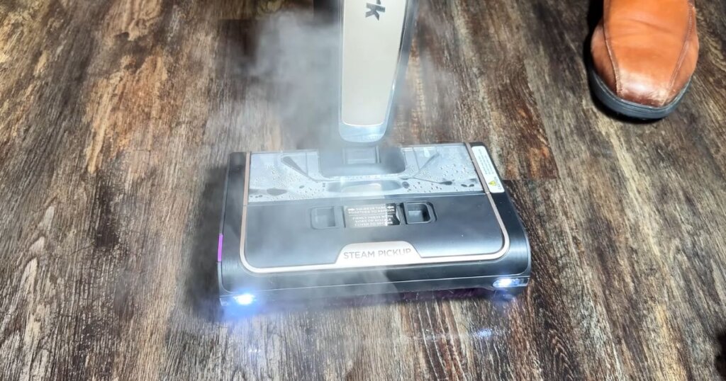 Shark Steam Pickup in use emitting visible steam on a hardwood floor, with lights on and a foot nearby.