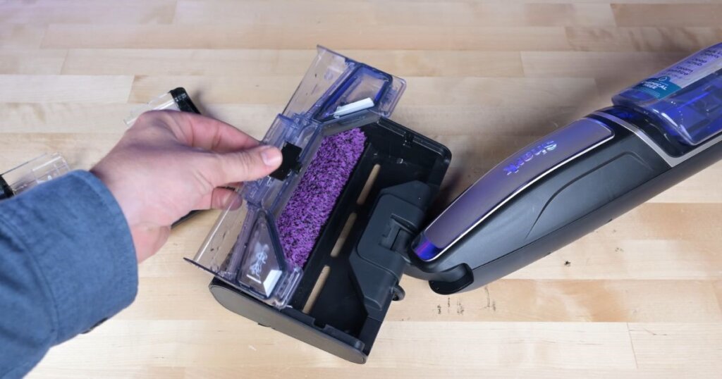 Hand removing the debris tray from the Shark Steam Pickup vacuum, showing internal roller and collection bin.
