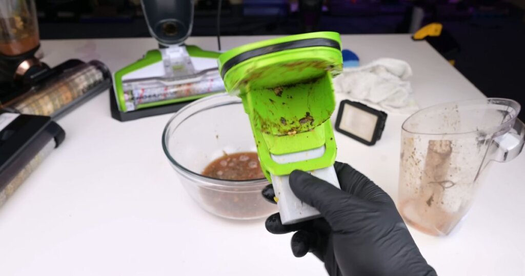Close-up of a dirty component from a green floor cleaner being emptied into a bowl of murky water during cleaning.