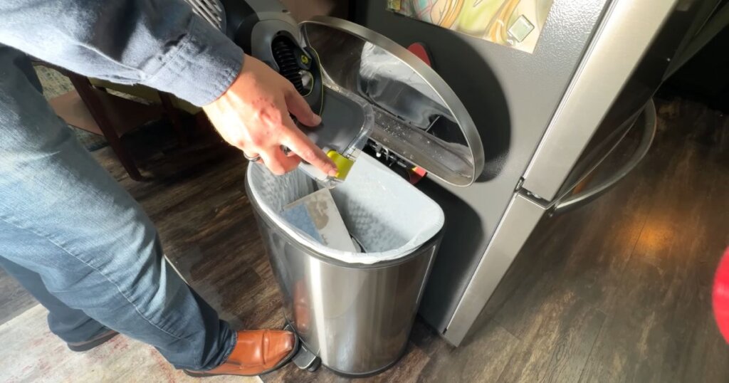 Person discarding a used Shark VACMOP cleaning pad into a kitchen trash bin.