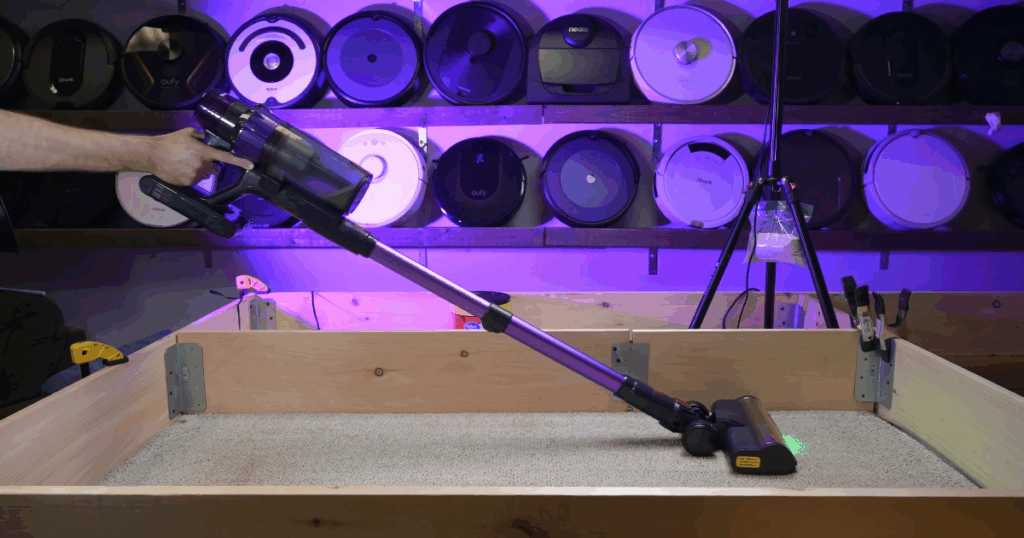 Action shot of the Smoture VAC02 being used in a Vacuum Wars carpet test setup with robotic vacuums in the background.